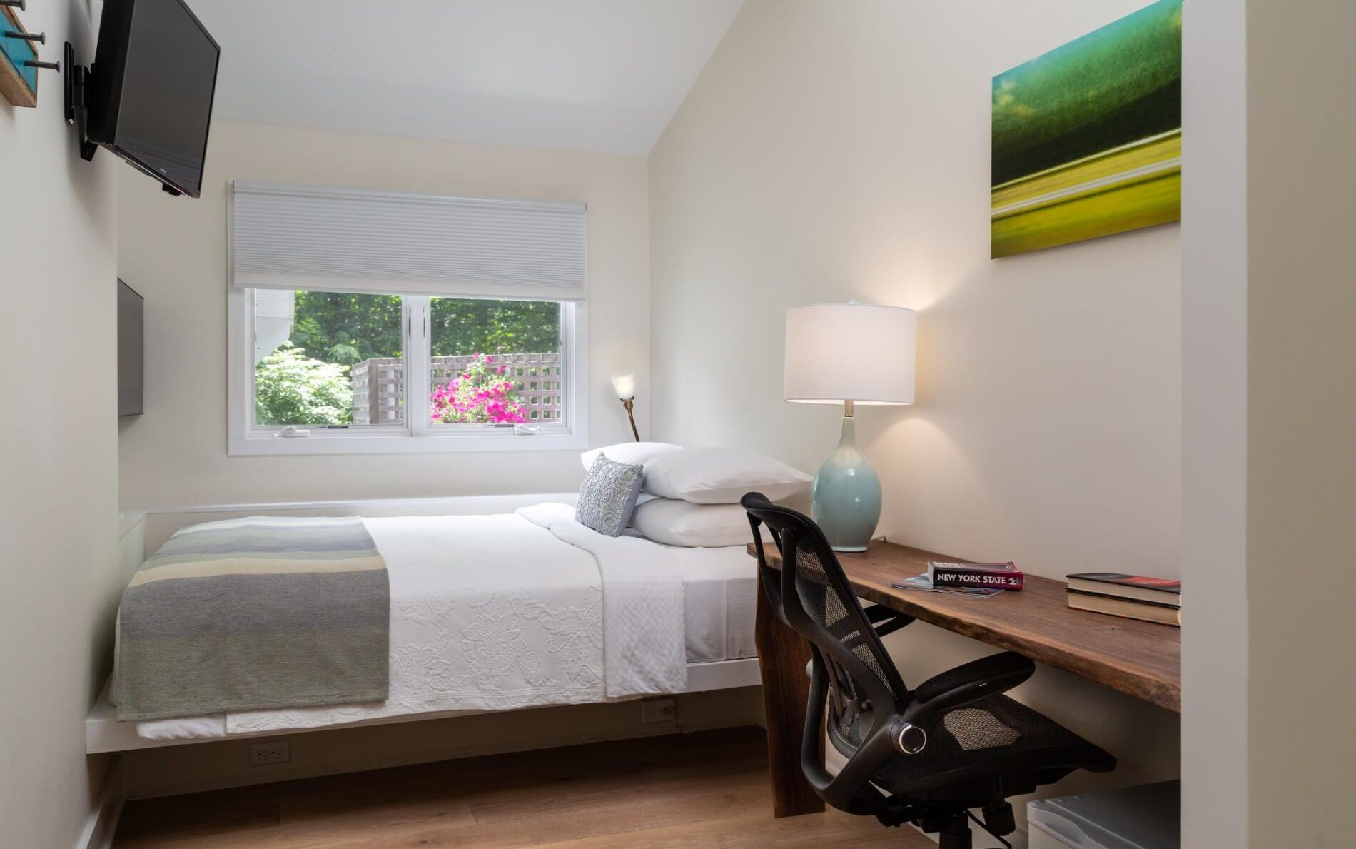 A narrow room with a desk on the right and a bed under the window.