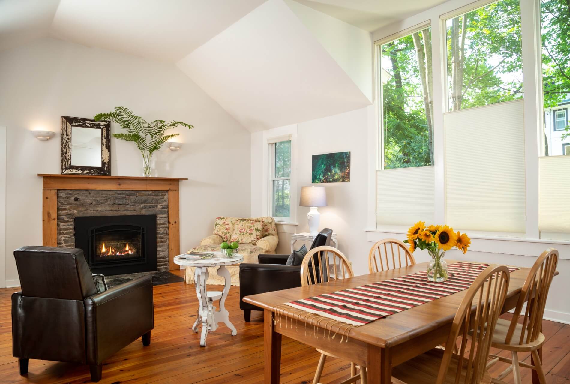 White room with an oak table and a stone fireplace. Leather chairs and a white table between them. 