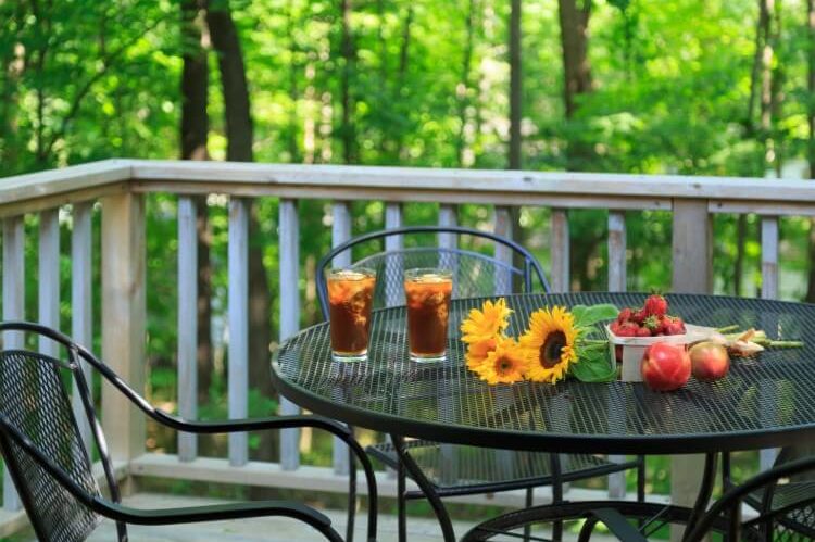 A patio table outdoors with flowers, drinks and fresh fruit.