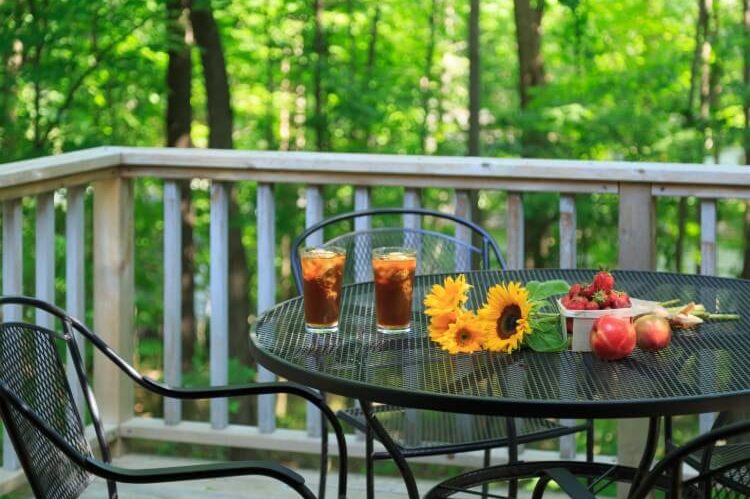 A patio table outdoors with flowers, drinks and fresh fruit.