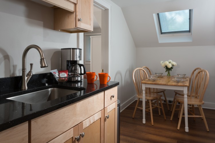 A black kitchen counter, coffee pot and dining table are part of the kitchen.