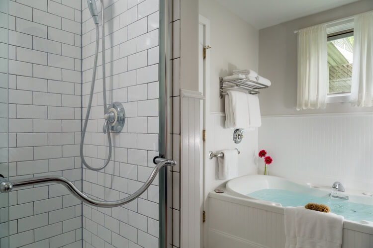 A shower with glass doors is on the left and a soaking tub with warm blue water is to the right. Everything in white tiles.