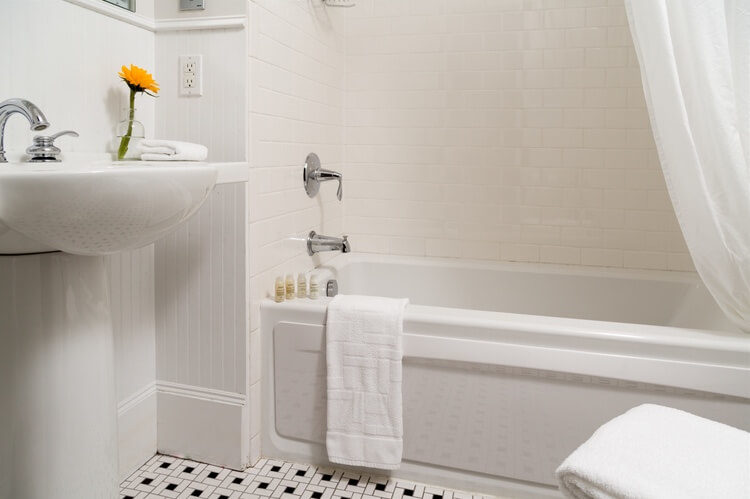 A hote sink a soaking tub sit upon a floor of white subway tiles, with black accents.