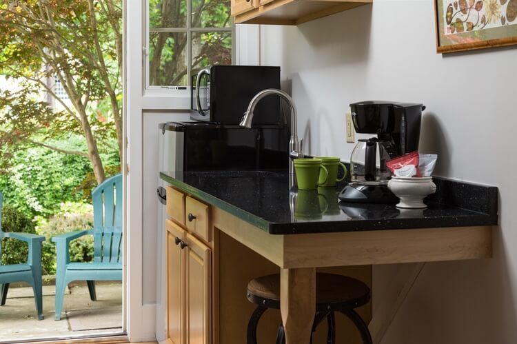 A black counter with sink and coffee pot, and brown cabinets are next to a window and a door the leads outdoors..