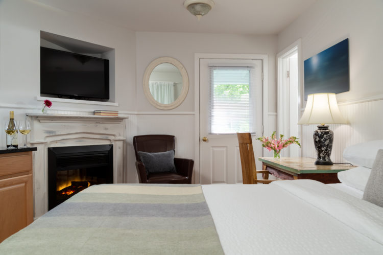 big bed with green blanket and a white-washed fireplace with a door and a window looking toward green trees