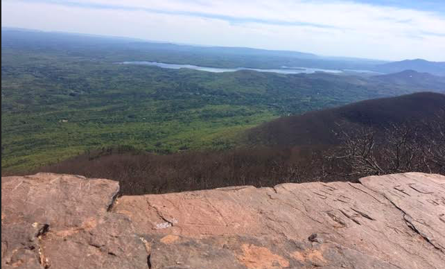 Brown rock in the foreground, light and dark green below and a river winding in the distance. 