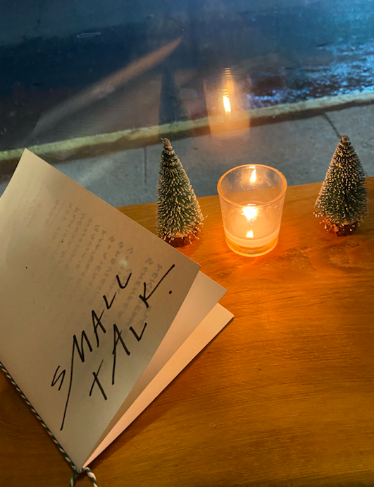 folded paper menu with a small candle and two tiny Christmas trees on a wooden table
