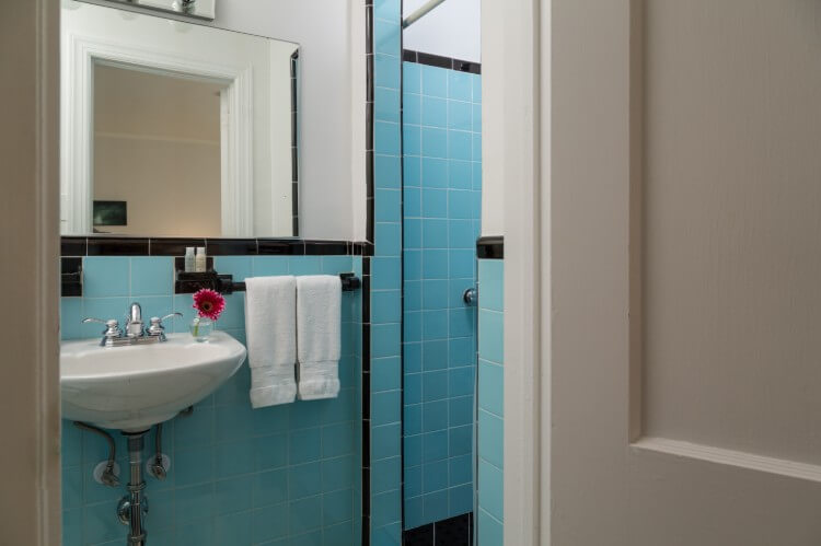 a white sink, plue tiles trimmed in black open to a shower area.