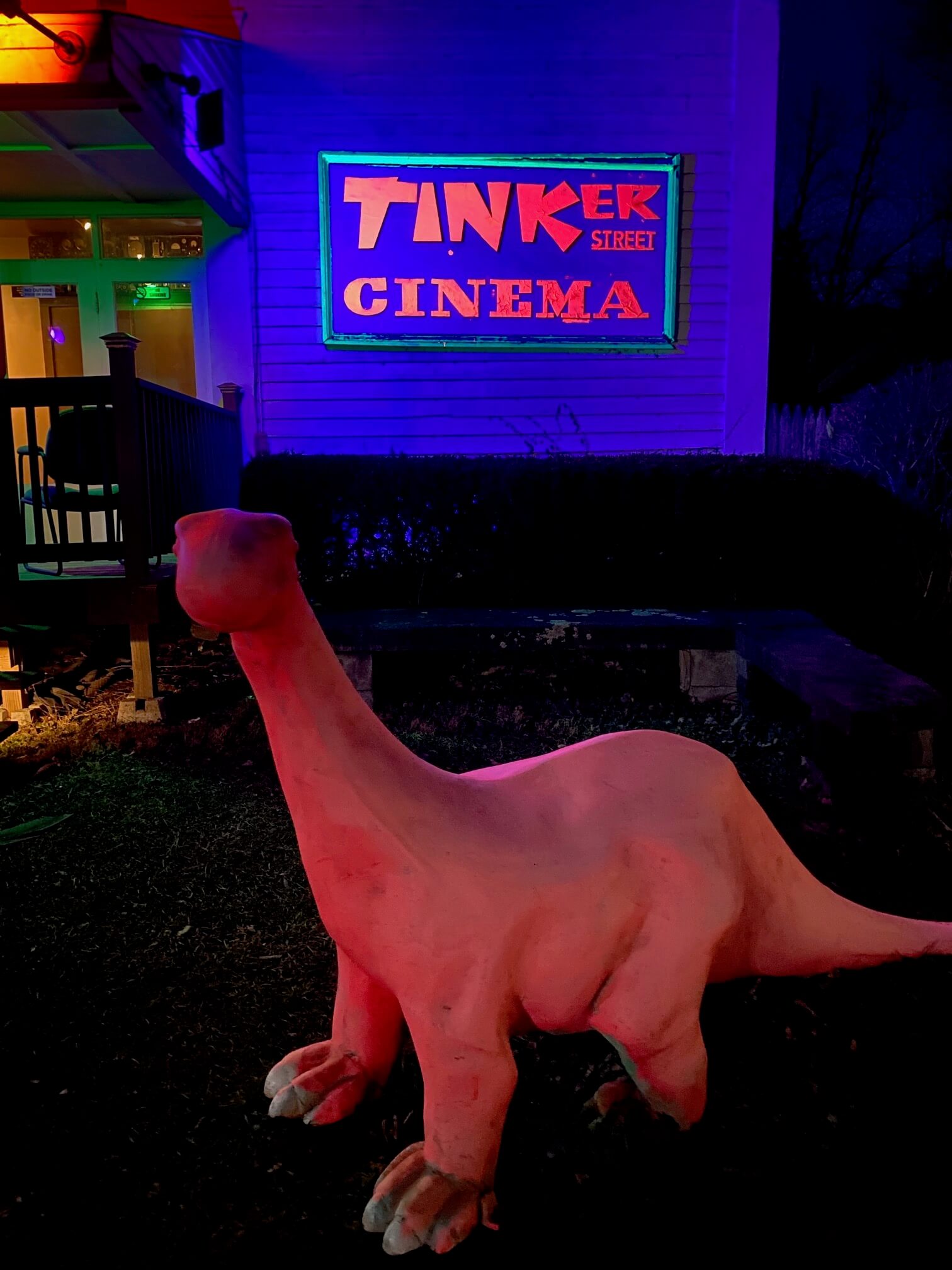 A pink dinosaur in front of a neon sign that says Tinker Cinema. 