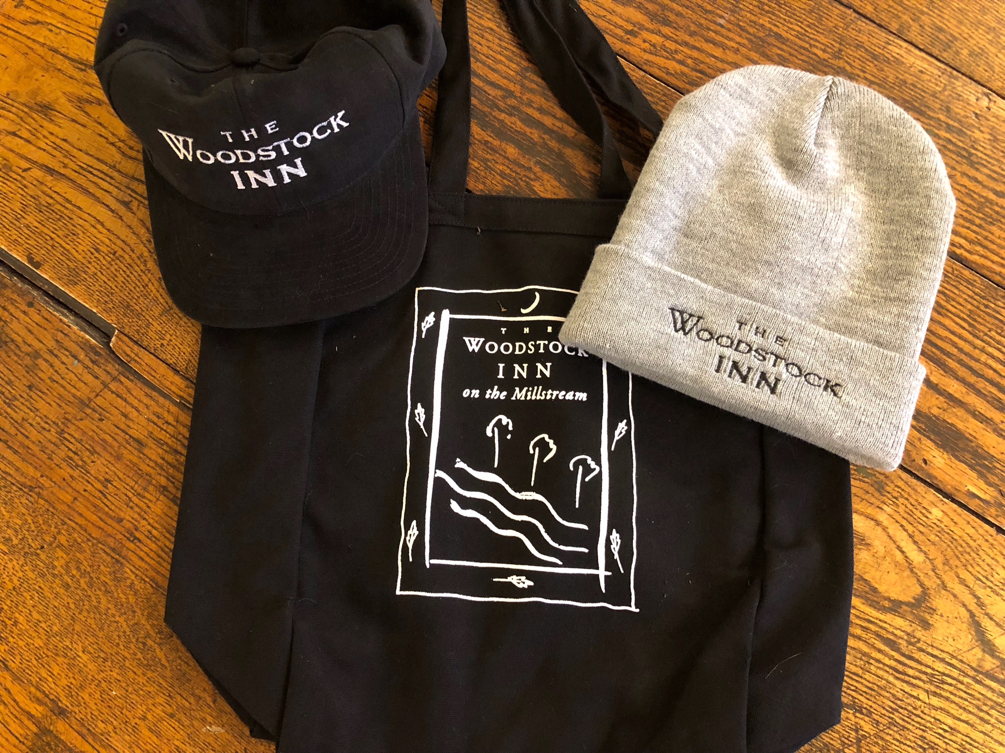 a black hat, black tote bag and a gray beanie hat, all have the woodstock inn logo on them.