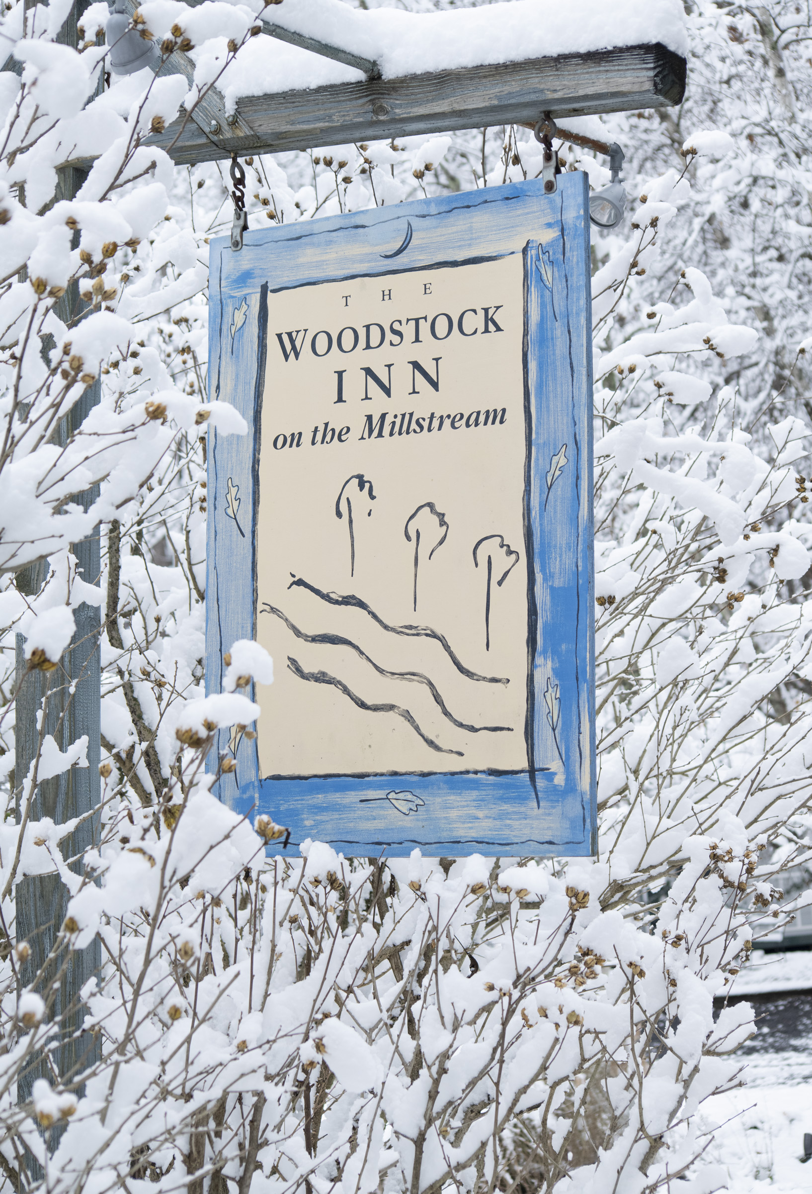 blue sign covered in snowy branches says Woodstock Inn on the Millstream 