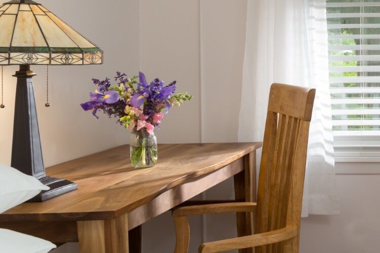 A wooden desk and chair, with flowers by a window.