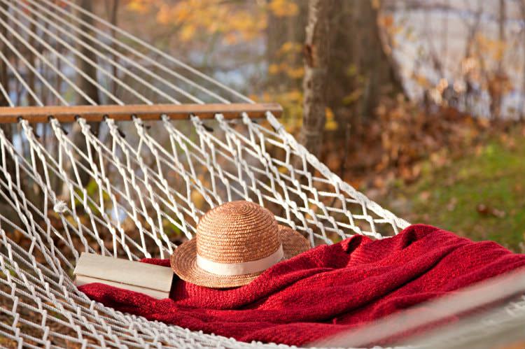 White netted hammock topped with straw hat, red blanket and book surrounded by autumn trees