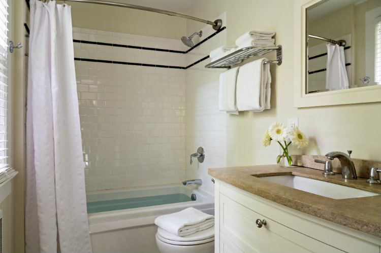 Beige and white bathroom with window, white towels, tan countertop, and curved shower rod with white curtain