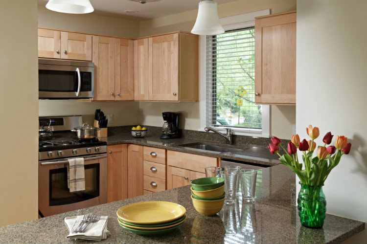 Beige kitchen with natural cabinetry, stainless steel appliances, window over the sink and granite tops