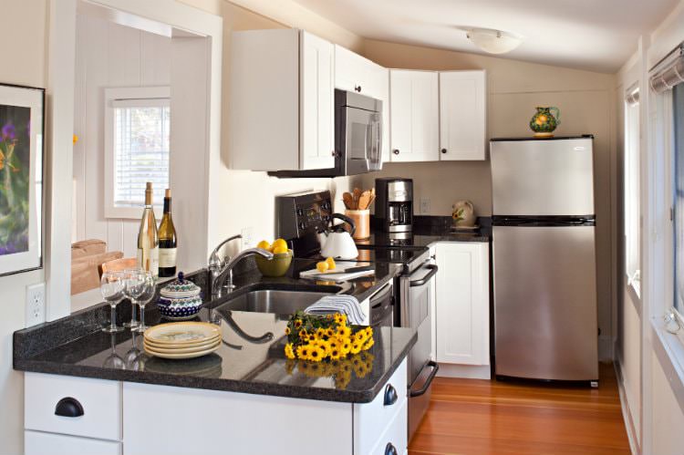 Beige and white kitchen with wood floors, stainless steel appliances, dark granite tops, and several windows