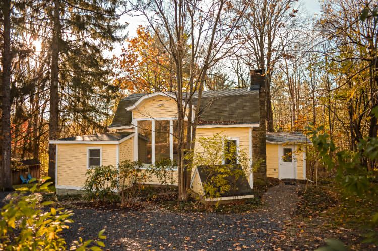 Yellow and white cottage in the woods full of trees losing their leaves