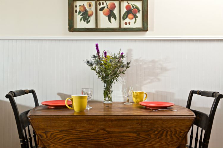 Wood drop-leaf table with two chairs, set for a meal and topped with fresh wildflowers