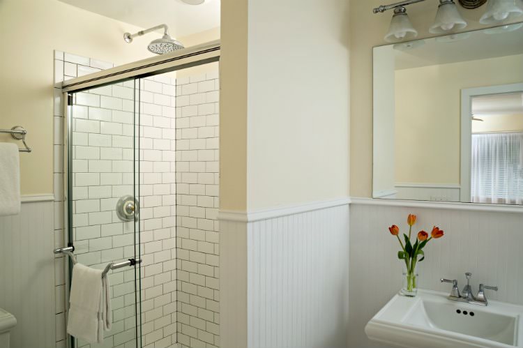 Beige and white bathroom with walk-in tiled shower with glass door, white pedestal sink, white towels and a window