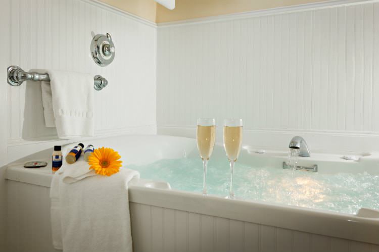 White whirlpool tub surrounded by white beadboard, with white towels and two champagne flutes