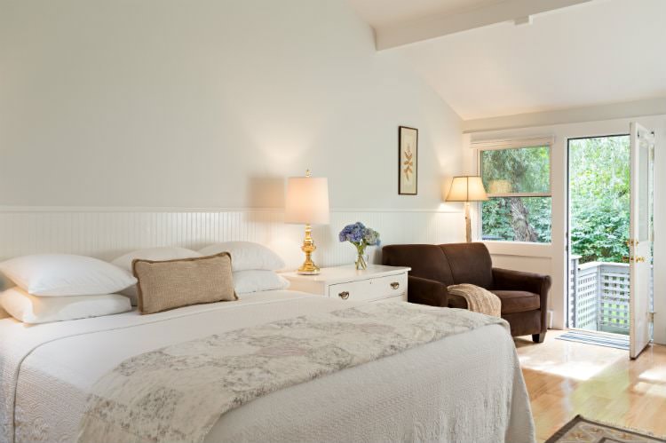 White vaulted room with hardwood floors, brown upholstered love seat, white quilted bed and lots of natural light