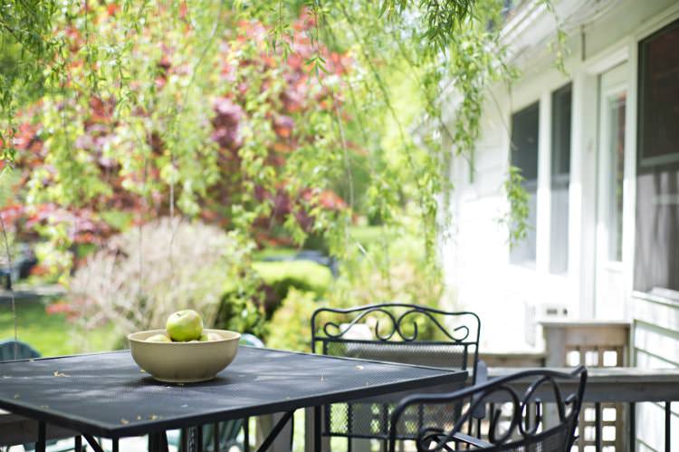 Black patio table and chairs with view of green grass and green and red leafed trees in background