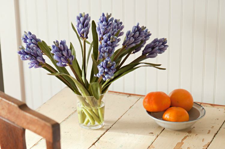 Rustic wood table topped with fresh purple flowers and bowl of fresh oranges