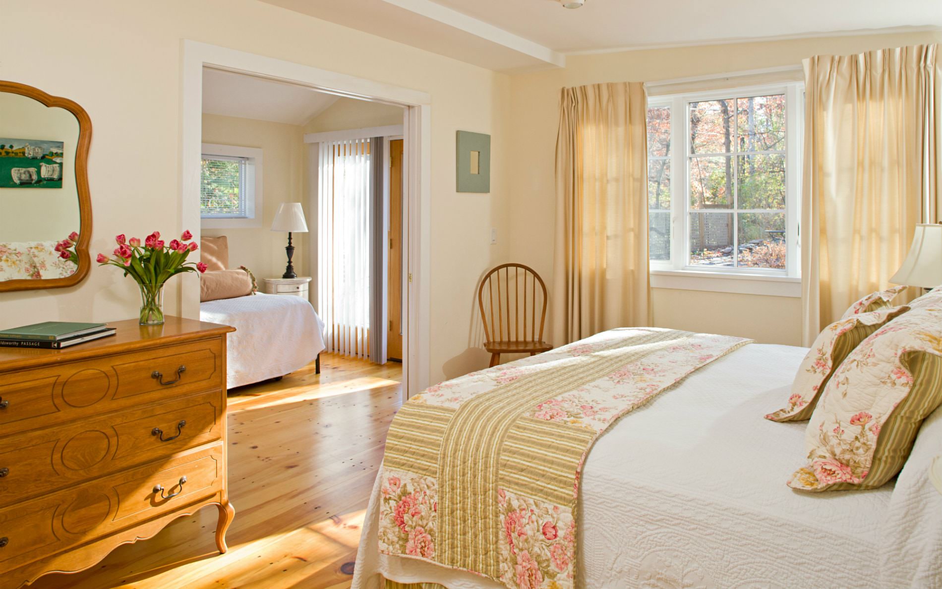 Warm and cozy beige and white adjoining rooms with wood floors, lots of natural light, and white covered beds