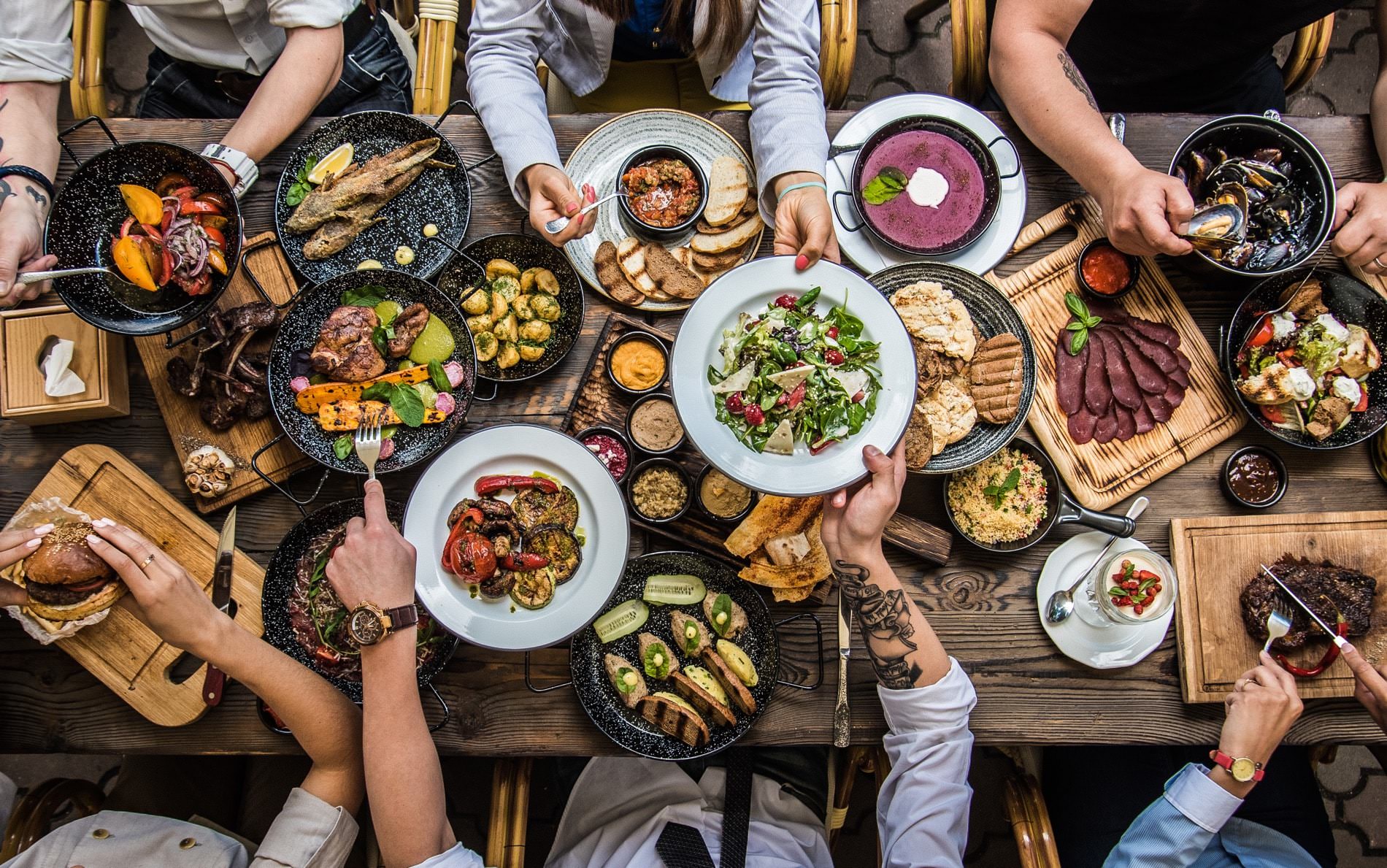 Overhead view of a group of people at a dining table sharing white and black plates of colorful prepared food