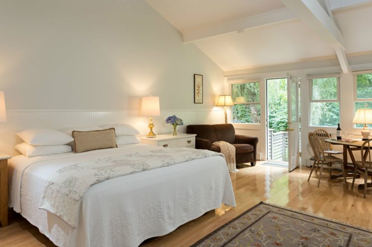 White vaulted room with wood floors, several windows, glass door, white covered bed, love seat, and table and chairs
