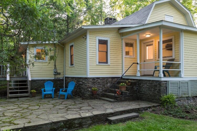 A bluestone patio wraps around a porch that has a door.
