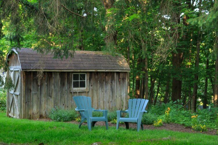 A green lawn with a brown barn and two blue chairs.