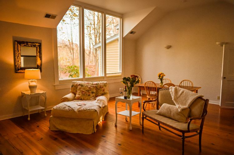 Cozy beige vaulted room with wood floors, large triple window, wood dining table and chairs, and sitting area