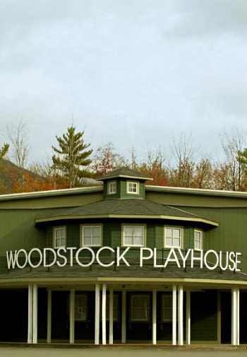 Exterior view of green and white Woodstock Playhouse surrounded by cloudy skies and autumn trees