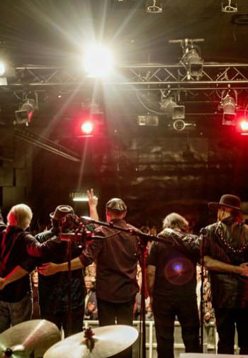 Backstage view of country band during an encore before an audience with white and red lights overhead