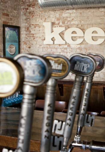 Close-up view of beer tap handles surrounded by white washed brick walls and dark wood tables and chairs