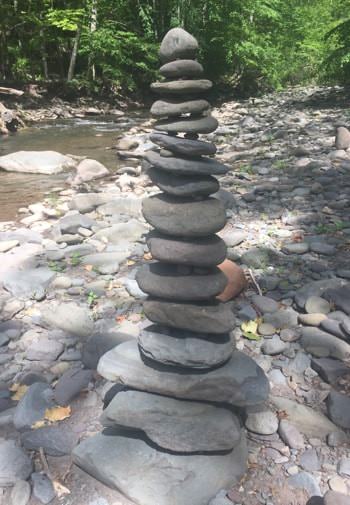 Stack of rocks surrounded by a bed of rocks , a stream, and green trees