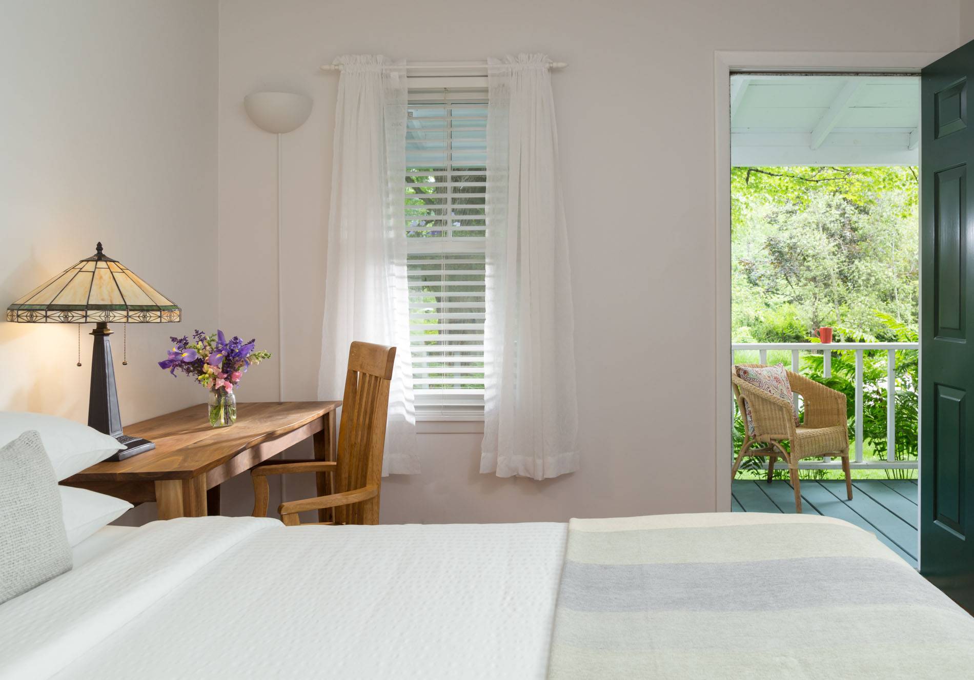 bed with white cover, brown desk, door opens outside 