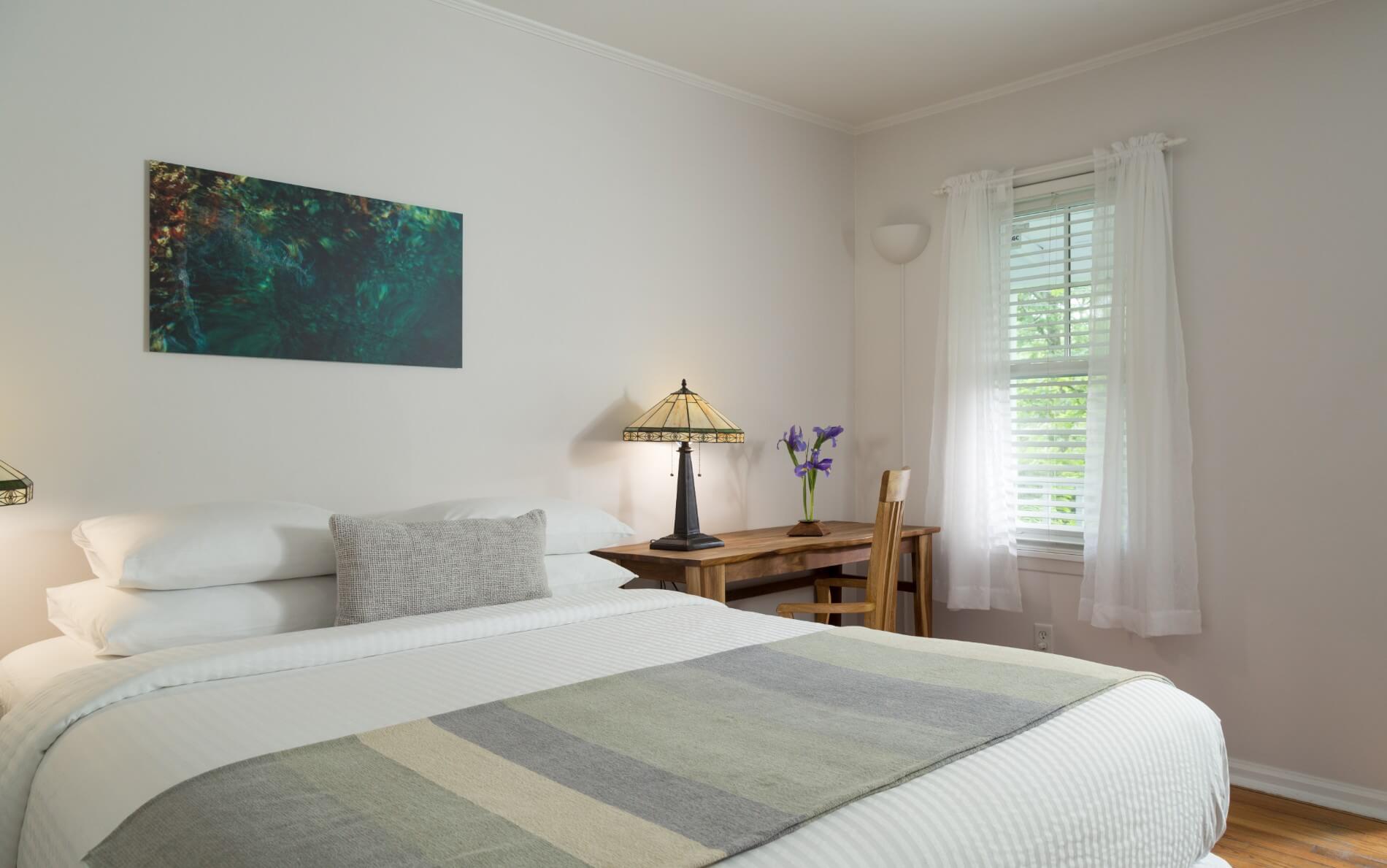 A large bed, with a blue gray striped blanket, desk and window.